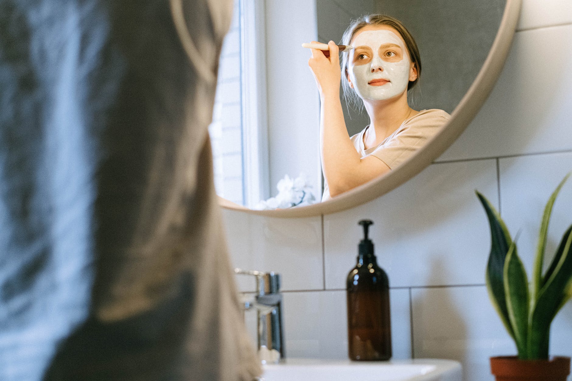 woman applying facial mask clay with a brush in front of mirror