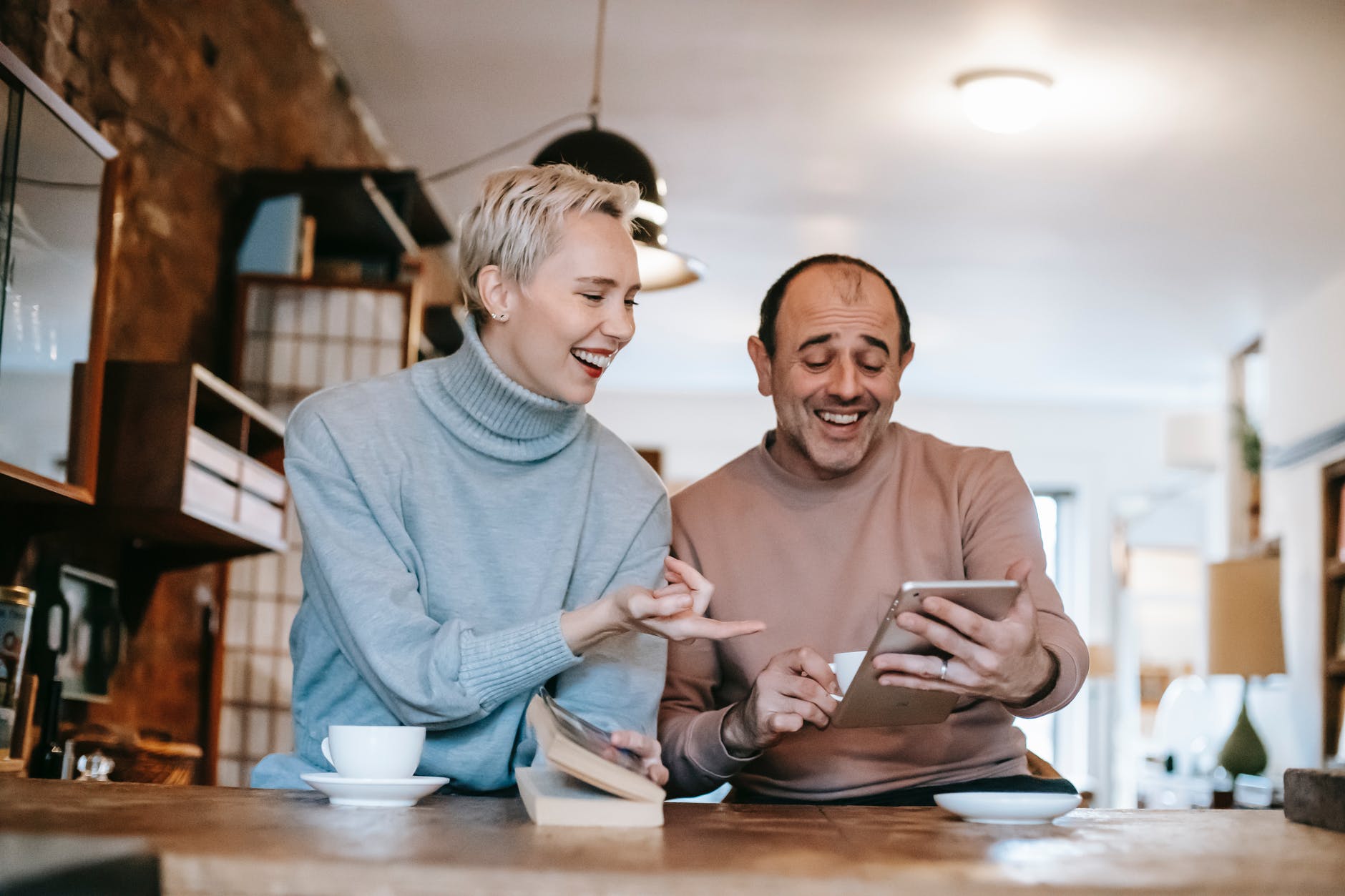 joyful multiracial spouses laughing while watching funny movie on tablet
