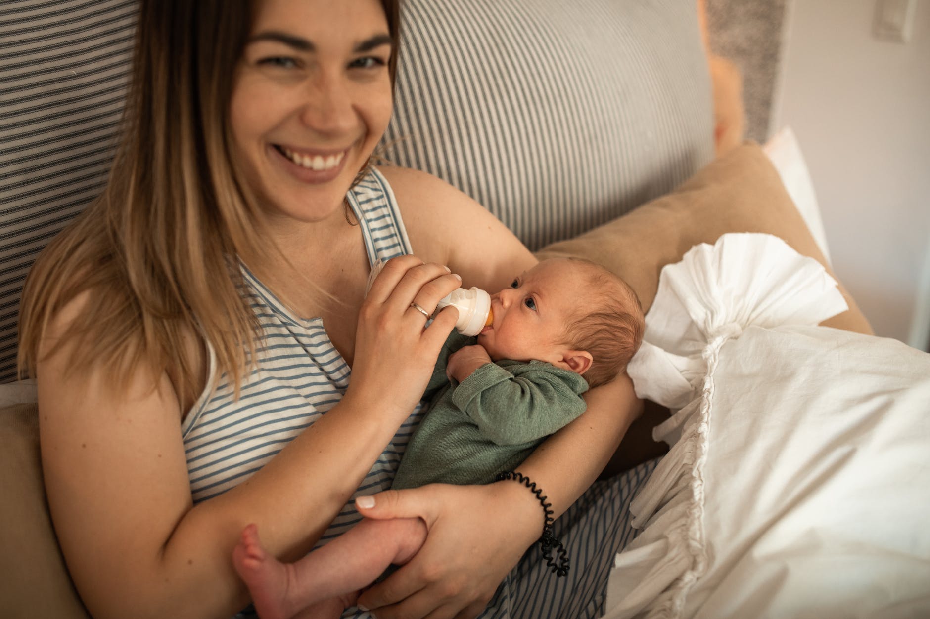 a woman smiling while feeding her baby with milk bottle