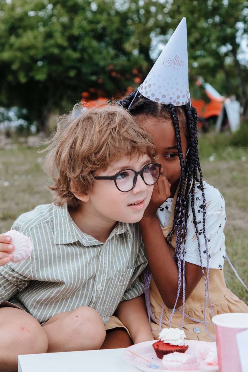 girl whispering to boys ear at birthday party in garden