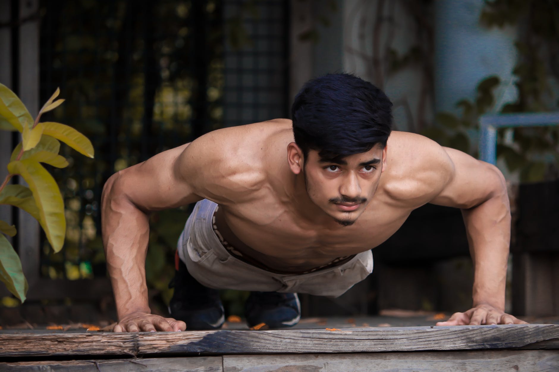 man in white tank top and blue denim jeans sitting on brown wooden bench