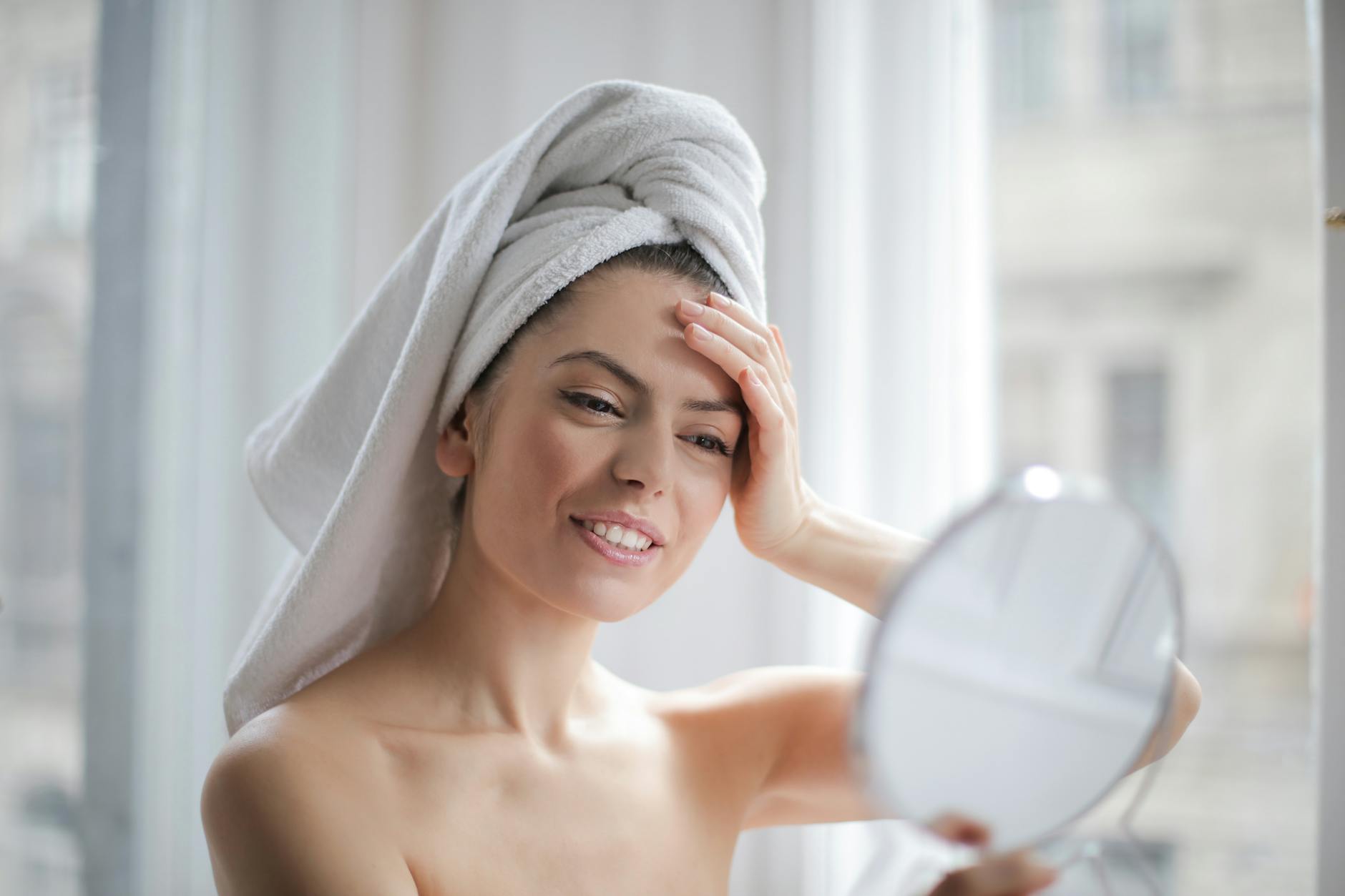 selective focus portrait photo of smiling woman with a towel on head looking in the mirror