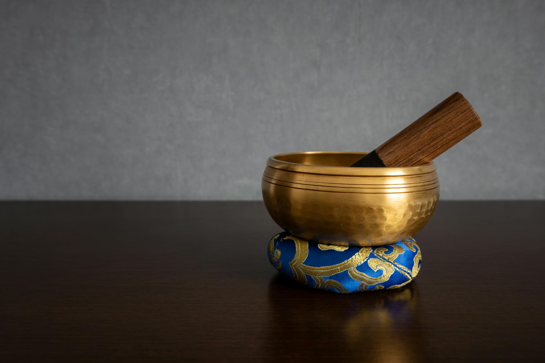 a golden colored tibetan singing bowl with striker inside standing on a ring cushion isolated on a blurred clean background and empty space for text spirituality and meditation concept