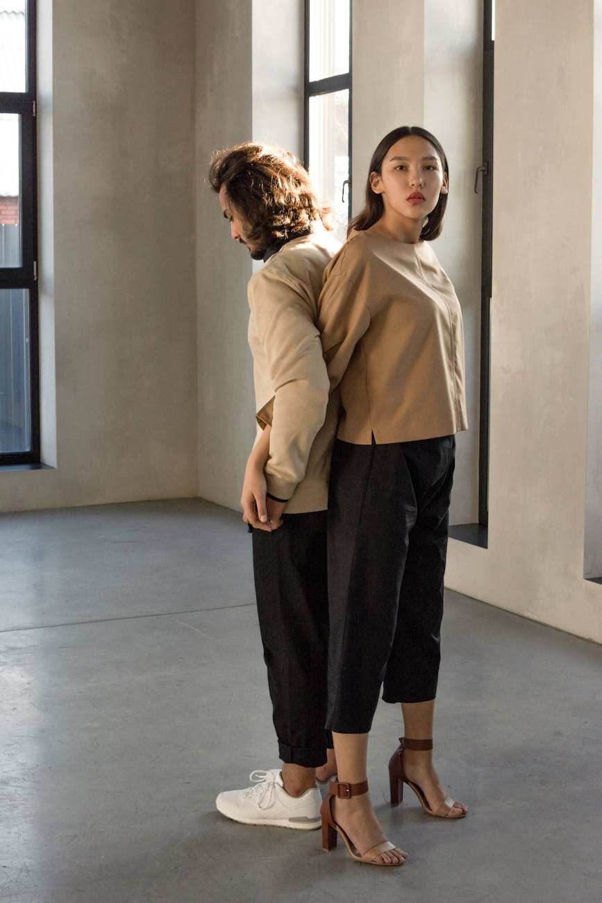 man and woman in beige long sleeve shirt and black pants standing back to back